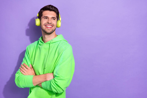 Photo of glad interested guy with brunet hairdo dressed green hoodie headphones look empty space isolated on purple color background. - Foto, afbeelding