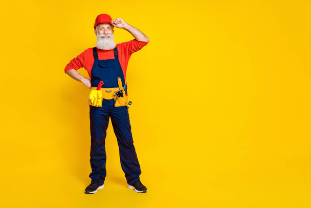 Full body photo of handsome grandpa builder arm touch hardhat toolbelt wear blue workwear overall red helmet isolated on yellow background. - Foto, Imagem