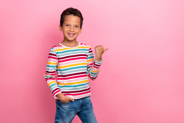 Photo of cheerful pupil latin small boy point empty space hold hand pocket dressed trendy striped look isolated on pink color background. - Photo, image