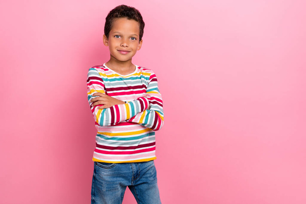 Zdjęcie słodkiego uroczego chłopca z falowaną fryzurą nosić paski długie rękawy ramiona skrzyżowane uśmiechając się odizolowany na różowy kolor tła. - Zdjęcie, obraz