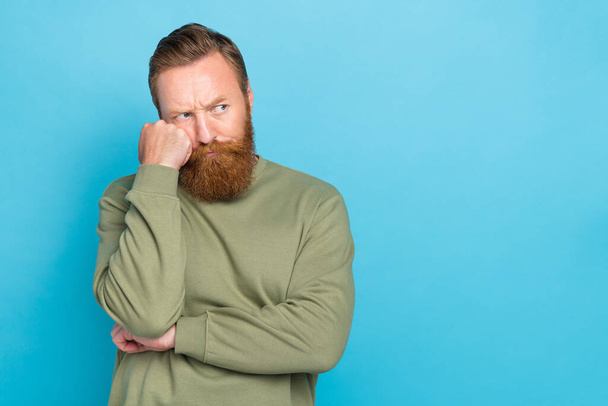 Photo of serious handsome guy with ginger hairdo khaki long sleeve look empty space hand on cheekbone isolated on blue color background. - Foto, afbeelding