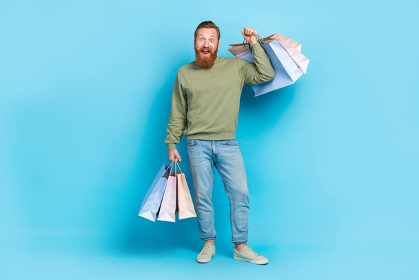 Full size photo of attractive young guy excited hold shopping bags big sales discount wear khaki clothes isolated on cyan color background. - Foto, Imagem