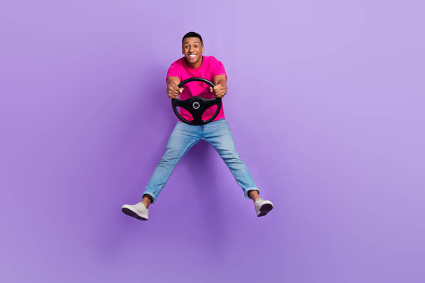 Full body photo of excited cheerful person jumping hands hold wheel isolated on violet color background. - Foto, afbeelding