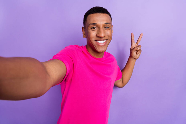 Foto di positivo allegro ottimistico ragazzo casella taglio di capelli vestito rosa t-shirt spettacolo v-segno facendo selfie isolato su sfondo di colore viola. - Foto, immagini