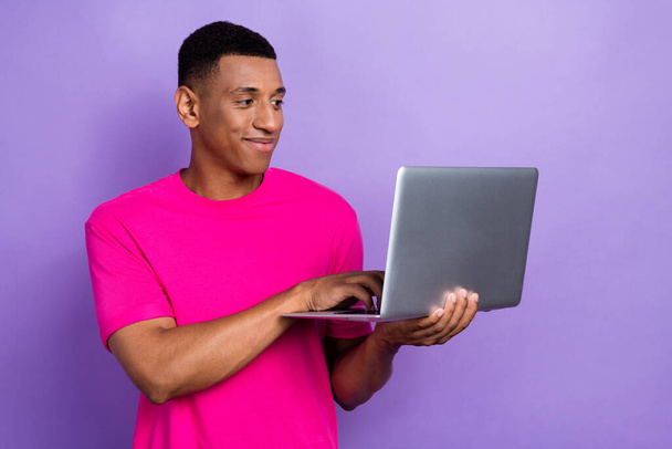 Photo of optimistic cheerful busy guy with box haircut dressed pink t-shirt typing code on laptop isolated on purple color background. - Φωτογραφία, εικόνα