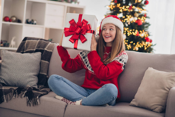 Full size photo of cheerful positive girl sitting couch arms hold newyear giftbox garland lights indoors. - Фото, изображение