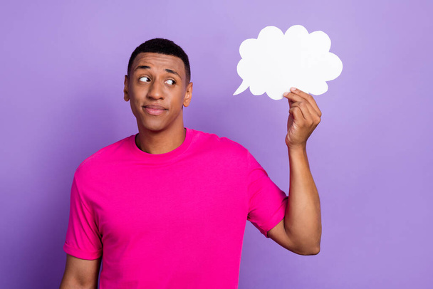 Photo of young unsure ponder serious guy wear pink bright t-shirt looking interested white paper cloud choice idea plan isolated on violet color background. - Foto, immagini