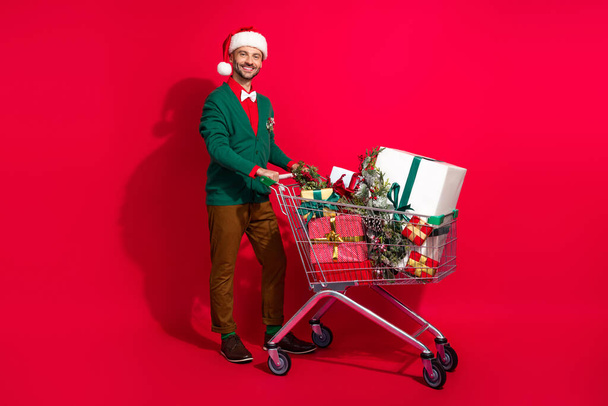 Full length photo of cute man wear x-mas green cardigan buying tray noel presents bargains isolated red color background. - Φωτογραφία, εικόνα