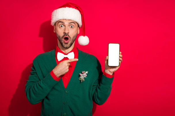 Photo of shocked excited man wear x-mas bowtie green cardigan pointing modern device empty space isolated red color background. - Φωτογραφία, εικόνα