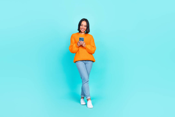 Full length photo of charming adorable girl dressed orange pullover typing modern gadget isolated teal color background. - Photo, Image