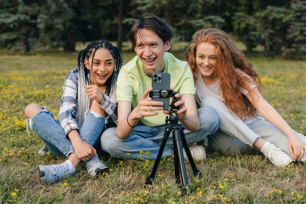 Group of friends taking selfie using a mobile phone on a tripod in the summer park. Summer nature. People lifestyle. Happy lifestyle. - Photo, Image