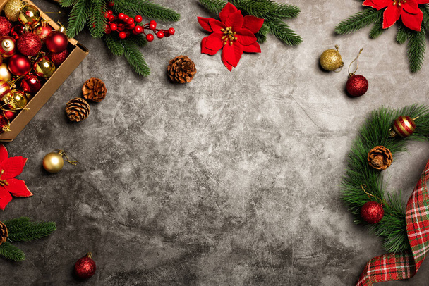 Χριστουγεννιάτικο στεφάνι σε πέτρινο τραπεζάκι. Κουτί με χριστουγεννιάτικα κόκκινα και χρυσά στολίδια. Χαιρετισμός Κάρτα φόντο με κλαδιά έλατο και Poinsettias - Φωτογραφία, εικόνα