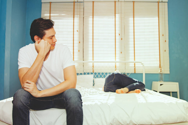 Husband who wants to have upset sex sits upset bored unhappy and uses consciousness to look at his frail wife lying sick with fever during the menstrual period, lying sick, recuperating and sleeping. - 写真・画像