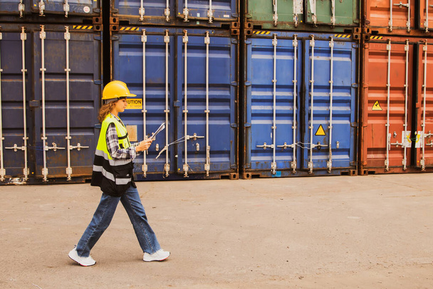 Oldalnézet női kaukázusi mérnök munkás visel biztonsági sisak gazdaság vágólap séta ellenőrzése rakomány konténer raktár rakodóudvar export ipar logisztikai üzlet. - Fotó, kép