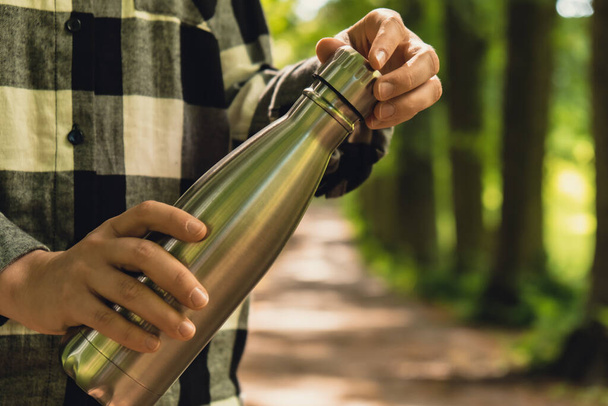 Close-up of Unrecognizable female hand holding Water bottle. Reusable steel thermo water bottle in park. Sustainable lifestyle. Plastic free zero waste free living. Go green Environment protection - Fotografie, Obrázek