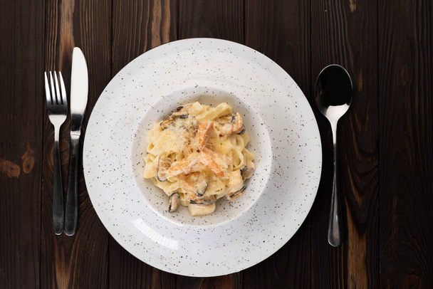 パスタの上にエビのアルフレド、ムール貝とクリームソースとおいしいイタリアのパスタのプレート、トップビュー。木の背景に。イタリア料理のコンセプト - 写真・画像