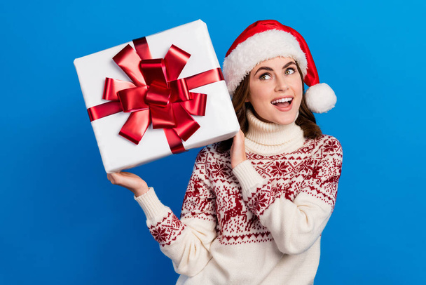 Photo of pretty cheerful astonished positive lady wear cozy ugly sweater think what inside gift box isolated on blue color background. - Foto, imagen