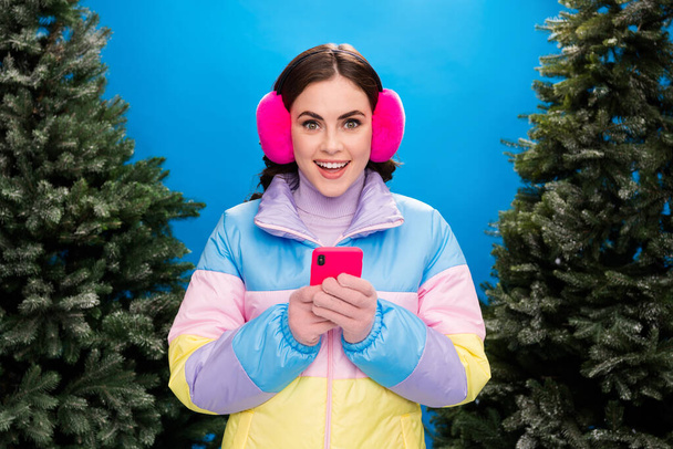 Photo of excited sweet girl dressed windbreaker typing instagram twitter facebook gadget outdoors isolated blue color background. - Foto, immagini