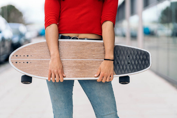 Unrecognized casual girl standing in the street holding her brown long-board. - Foto, imagen