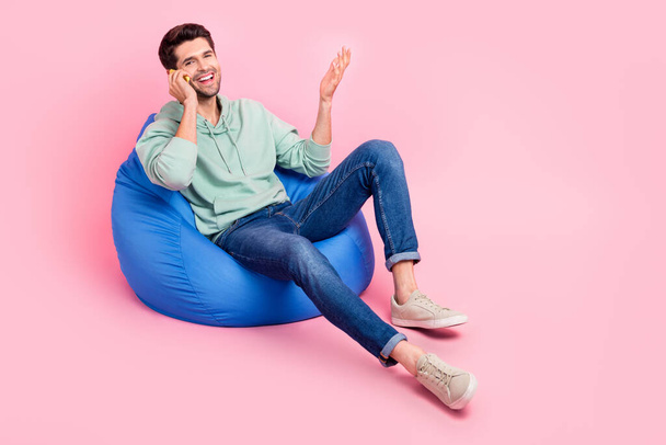 Full length photo of positive man sit chair use modern telephone chatting communicating empty space isolated on pink color background. - Foto, Imagen