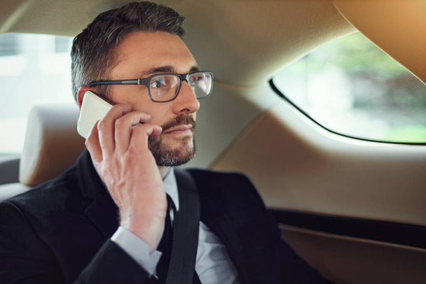 Calling his secretary to set up his appointments for the day. a businessman using his cellphone while sitting in the backseat of a car - Photo, Image