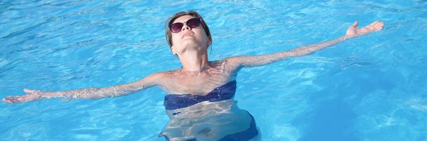 Young woman in sunglasses swimming and relaxing in pool top view. Vacation at resort concept - Photo, Image