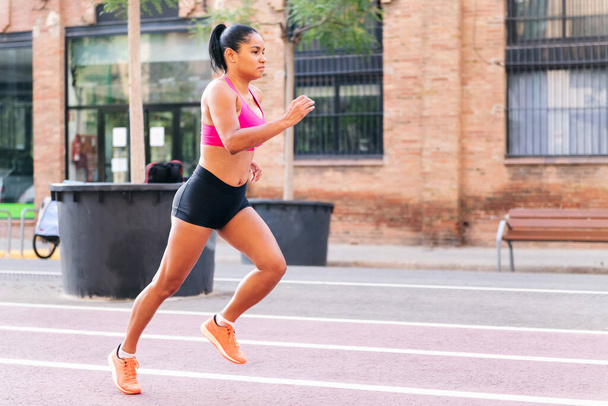 sportswoman running on the citys athletics track during her workout, urban sport and healthy lifestyle concept, copy space for text - Photo, Image