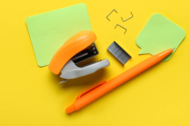Συρραπτικά, συνδετήρες, στυλό και αυτοκόλλητες σημειώσεις σε κίτρινο φόντο - Φωτογραφία, εικόνα