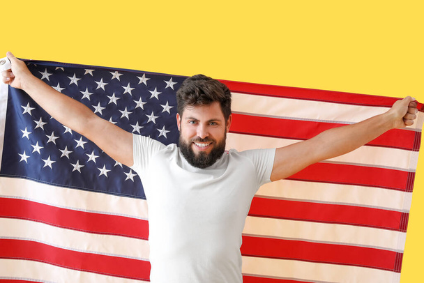 Sarı arka planda Amerikan bayrağı taşıyan yakışıklı sakallı adam. - Fotoğraf, Görsel