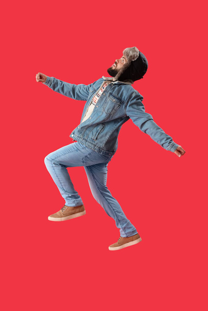 Komea mies lämpimässä hatussa hyppää punaisella taustalla - Valokuva, kuva