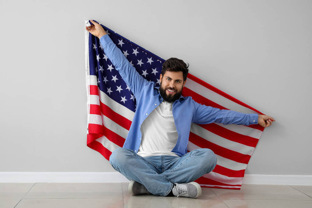 Όμορφος γενειοφόρος άνδρας με σημαία των ΗΠΑ κάθεται κοντά σε γκρίζο τοίχο - Φωτογραφία, εικόνα
