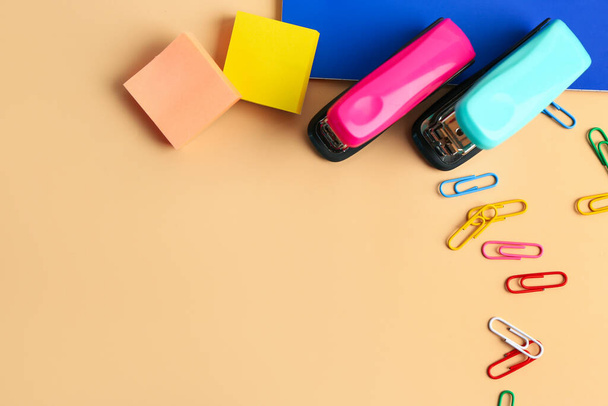 Office staplers, paper clips and sticky notes on color background - Photo, Image
