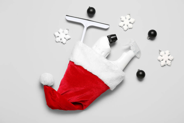 Καπέλο Σάντα με είδη καθαρισμού και χριστουγεννιάτικη διακόσμηση σε γκρι φόντο - Φωτογραφία, εικόνα
