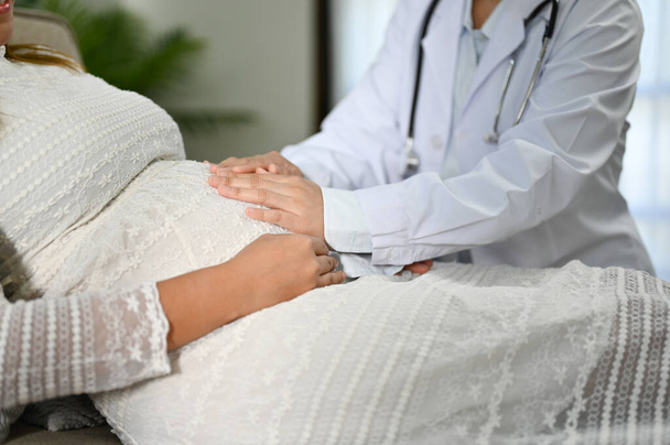 Profesyonel kadın doktor ya da kadın doğum uzmanı hastasını kontrol ediyor, hamile hastasının karnına dokunuyor. Görüntüyü yaklaştır. Antenatal bakım kavramı - Fotoğraf, Görsel