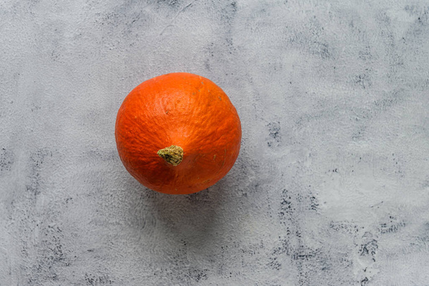 Pequeña, madura, hermosa, deliciosa calabaza naranja acostada sobre un fondo rústico gris. Mucho espacio de copia alrededor de la calabaza - Foto, Imagen