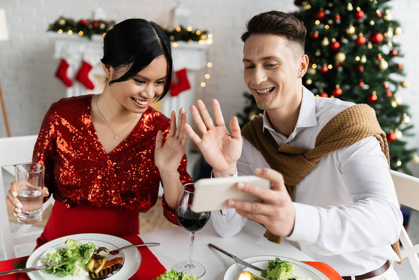 grávida asiático mulher com sorrindo marido acenando mãos durante vídeo chamada no smartphone no Natal celebração - Foto, Imagem