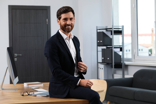 Smiling bearded man sitting on table in office - Foto, Imagen