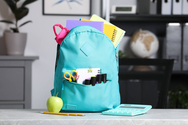Turquoise backpack and different school stationery on table indoors - Foto, Bild