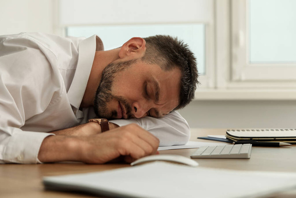 Tired man sleeping at workplace in office - 写真・画像