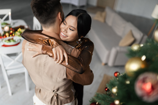 θέα από ψηλά χαρούμενη Ασιάτισσα που αγκαλιάζει τον άντρα της κατά τη διάρκεια των Χριστουγέννων - Φωτογραφία, εικόνα