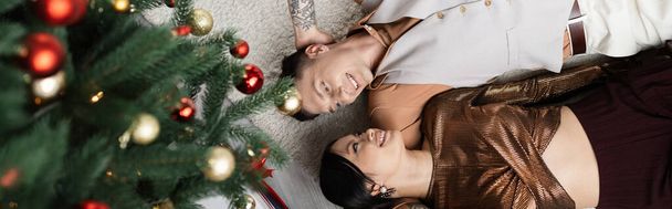 vista superior de pareja interracial feliz acostado bajo el árbol de Navidad, bandera - Foto, imagen
