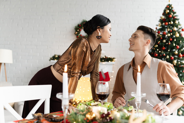 ευτυχισμένο διαφυλετικό ζευγάρι κοιτάζοντας ο ένας τον άλλο σχεδόν εορταστικό γεύμα την ημέρα των Χριστουγέννων - Φωτογραφία, εικόνα