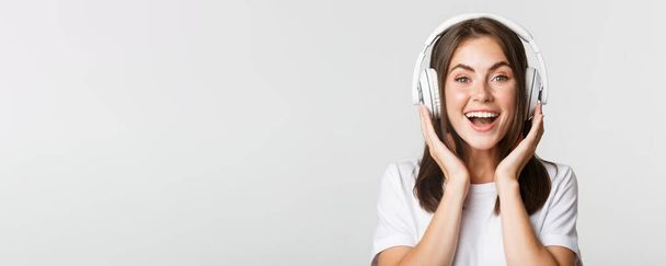 Primo piano di sorridere attraente ragazza bruna ascoltare musica in cuffia, godendo di podcast interessante. - Foto, immagini