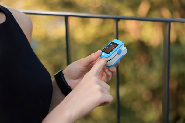 Woman checking pulse with blood pressure monitor on finger after training outdoors, closeup - Fotoğraf, Görsel