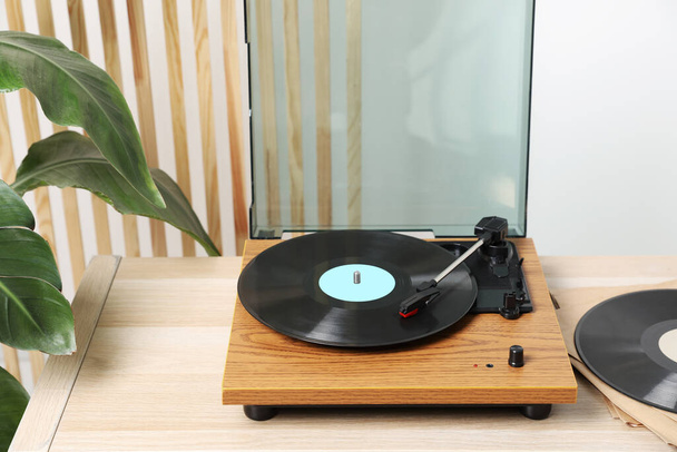 Stylischer Plattenspieler mit Vinylscheibe auf hellem Holztisch drinnen - Foto, Bild