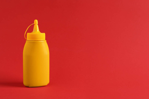 Spicy mustard in plastic bottle on red background, space for text - Zdjęcie, obraz