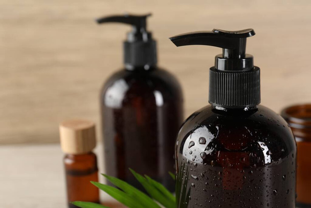 Shampoo bottles, essential oil and green leaf on white wooden table, closeup. Space for text - Foto, immagini