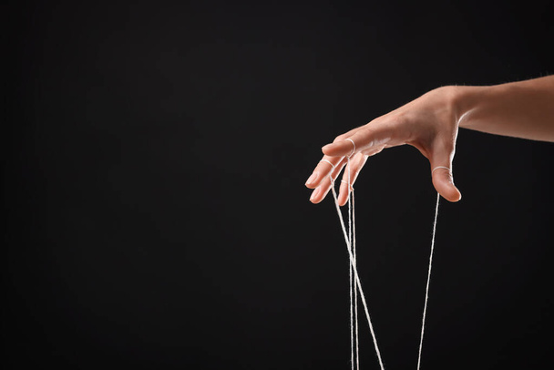 Woman pulling strings of puppet on black background, closeup. Space for text - Valokuva, kuva