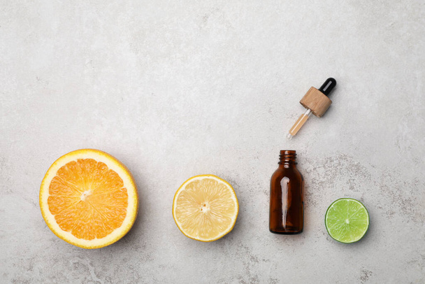 Bottle of citrus essential oil and fresh fruits on light table, flat lay. Space for text - Фото, изображение
