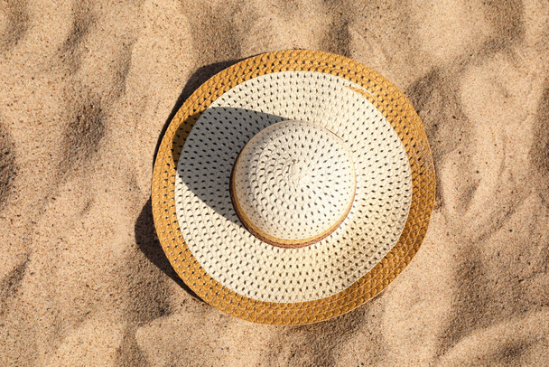 Beautiful beige straw hat on sand, top view - Foto, afbeelding